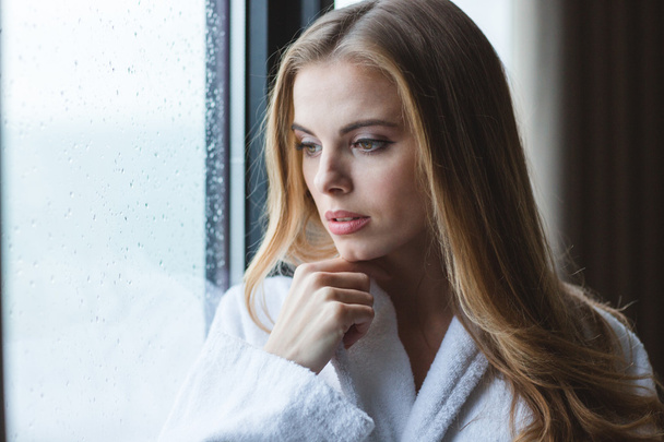 Attractive pensive young female in white bathrobe looking out  - Фото, зображення