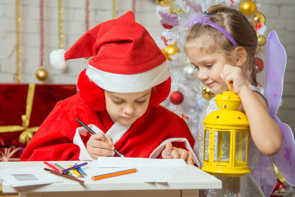 Chica vestida como Santa Claus firma el sobre con una carta, de pie junto a la chica de hadas con una linterna en la mano
 - Foto, imagen