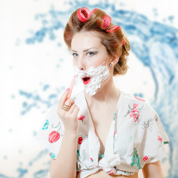 Beautiful young pinup woman shaving face with foam and razor - Photo, image