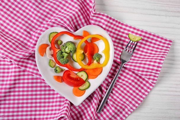 Useful cut vegetables on a plate in the form of heart on wooden table top view - Foto, imagen