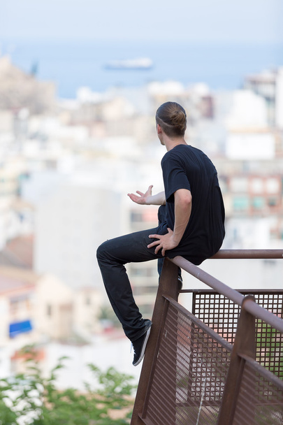 Rückansicht eines jungen Mannes, der auf einem Geländer sitzt - Foto, Bild