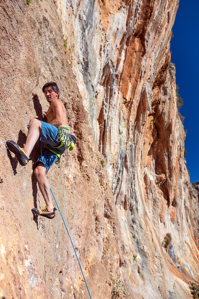 Альпинист на крутой высокой скалистой стене с шестеренкой оранжевого цвета камень
 - Фото, изображение