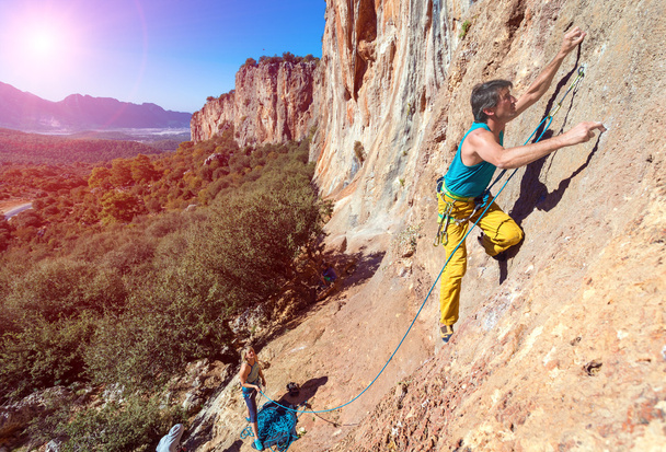 Команда альпинистов мужчина и женщина восходящие оранжевый яркий скалистый стены с веревкой и снаряжением
 - Фото, изображение
