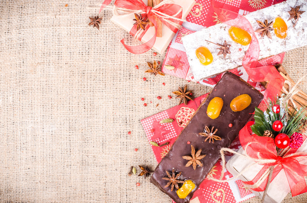 Chocolate spices cake, star anise and dried fruits, packed gifts with red tapes on sackcloth, canvas. Sweet frame. Free space for your text. - Foto, Imagen