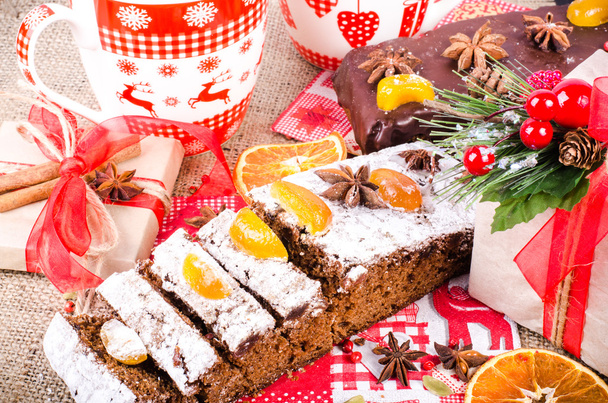 Chocolate spices cake, star anise and dried fruits, packed gifts with red tapes on sackcloth, canvas. Sweet frame. Top view - Fotografie, Obrázek