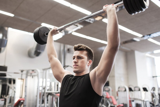young man flexing muscles with barbell in gym - Photo, image