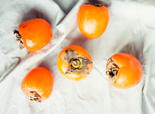 Fresh juicy persimmons on a light background, raw fruit - Фото, изображение