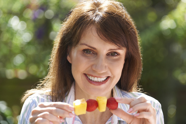 Middle Aged Woman Eating Fruit Kebab In Garden - Photo, Image