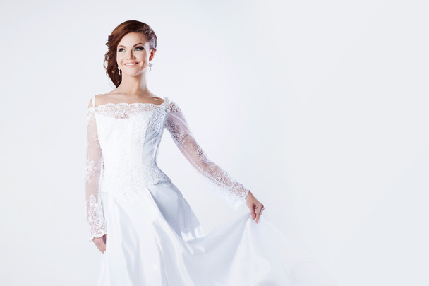 Beautiful bride in wedding dress, holds hem of dress and smiling, space for text on the right - Фото, зображення