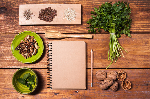 Notebook for recipes, walnuts, parsley and seeds on wooden table. - Φωτογραφία, εικόνα