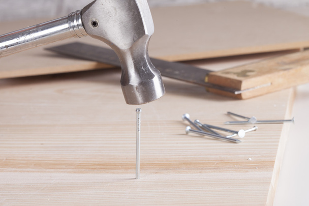 Close-up of metal hammer driving nail into wooden board - Zdjęcie, obraz