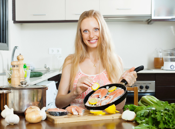 Smiling woman cooking salmon fish with lemon   - Фото, зображення