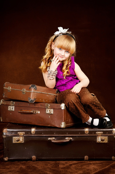 Young girl sits on vintage baggage against brown background - Foto, Imagem