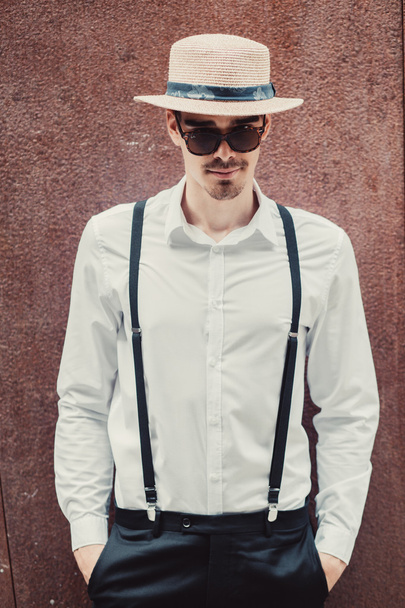 Joven modelo de hombre con estilo en sombrero y gafas de sol posando cerca de la pared. Moda tiro
 - Foto, Imagen