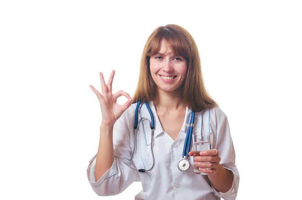 Ο γιατρός που κατέχει ένα ποτήρι με νερό στο χέρι και δείχνει ΟΚ. - Φωτογραφία, εικόνα