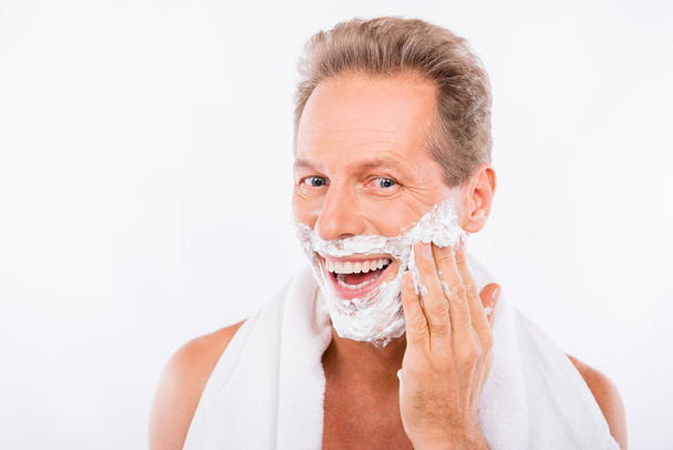 Handsome happy man with towel smearing shaving foam on his chin - Zdjęcie, obraz