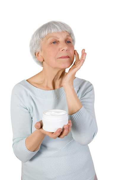 encantadora mulher idosa aplicando creme cosmético em seu rosto para cuidados com a pele facial em um fundo branco
 - Foto, Imagem