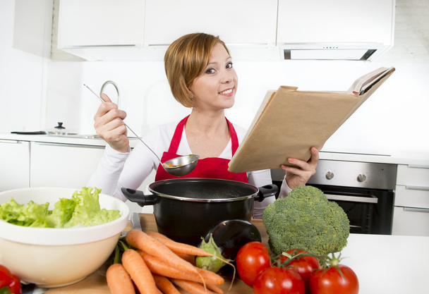 atractiva mujer cocinera preparando sopa de estofado de verduras lectura receta libro de cocina en la cocina doméstica
  - Foto, imagen