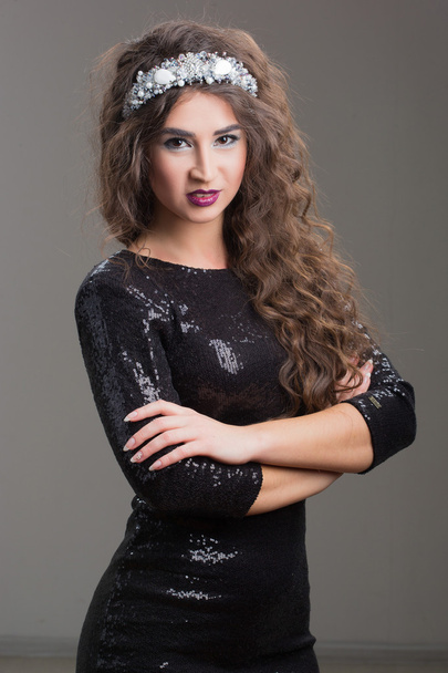 Beautiful fashion model posing in evening dress and in the diadem over dark background. - Фото, зображення