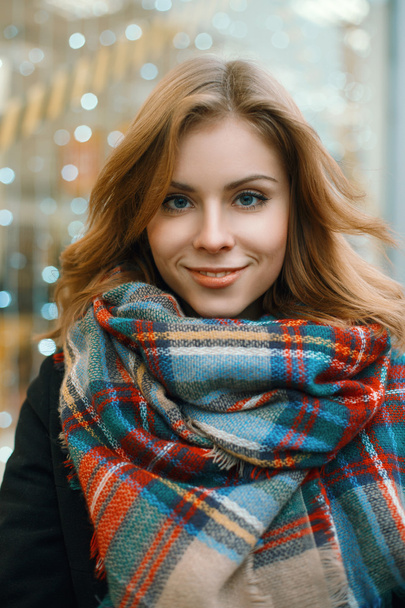 Close-up portrait of a beautiful woman in a stylish retro scarf and black coat on the background of showcases with lights - Foto, Bild
