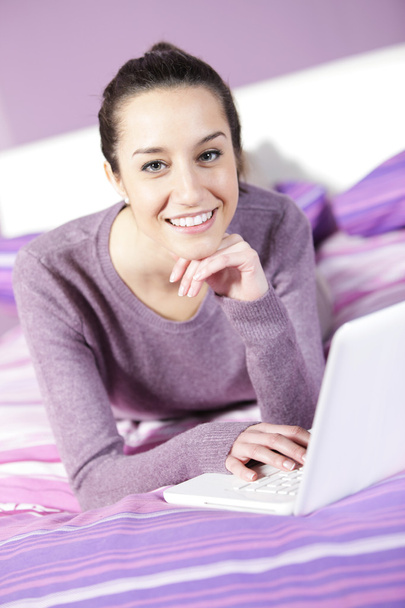 Portrait of a young female relaxing in bed while using laptop - Foto, Imagen