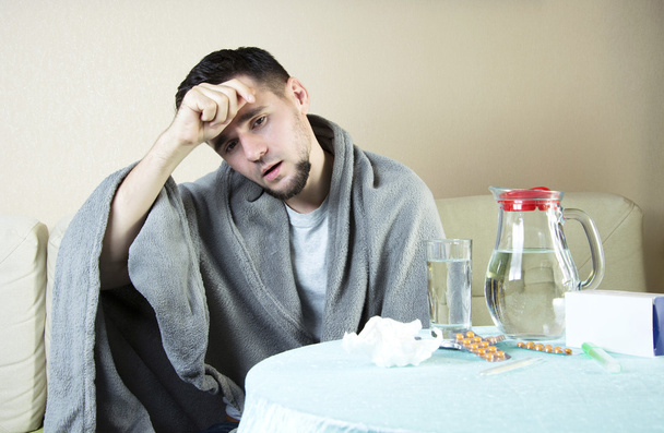 Porträt eines jungen Mannes auf Sofa mit Medikamenten und einem Glas Wasser.  - Foto, Bild