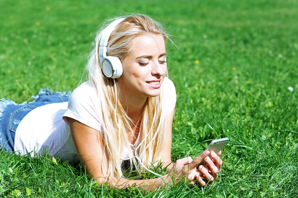 Young woman with earphones and smartphone listening to music on grass - Fotografie, Obrázek