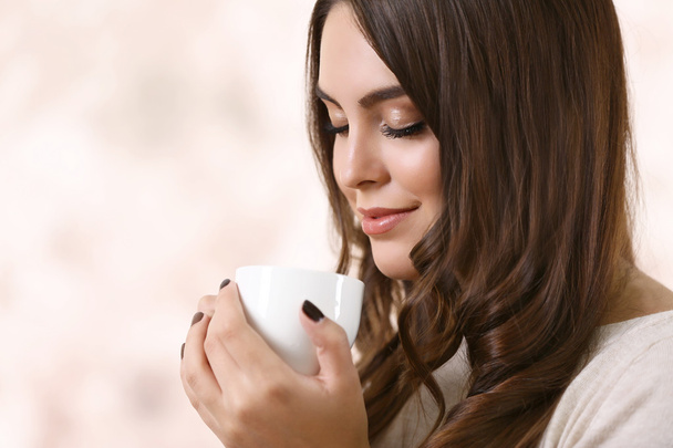 Portrait of young beautiful woman with cup of coffee on pink blurred background - Фото, изображение