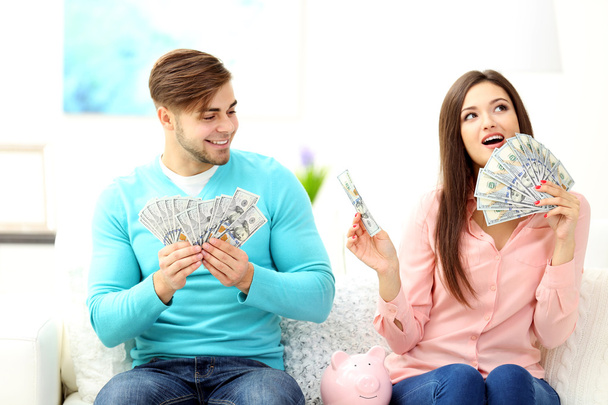 Happy couple sitting at home and counting money from the pig money box - Photo, Image