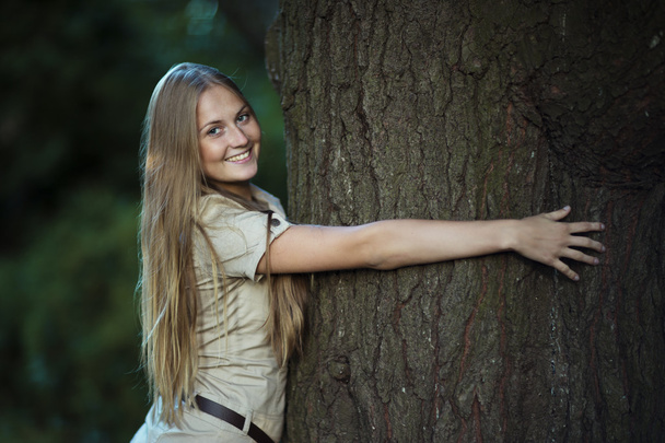 Young attractive girl hugging a big tree in park and smiling - Foto, Bild