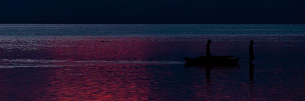 Σιλουέτα του δύο ψαράδες έξω στη θάλασσα μπλε πορφυρό ηλιοβασίλεμα - Φωτογραφία, εικόνα