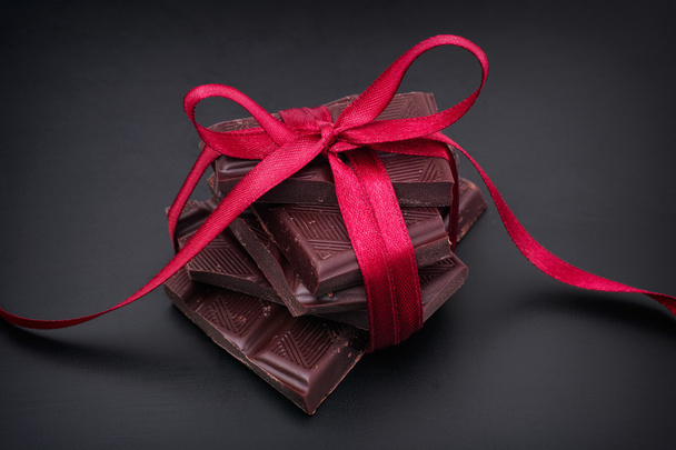 Dark chocolate with red ribbon on black background - Photo, image