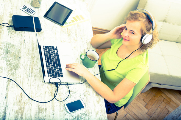 Young plus size woman listening to Audio while working on a lapt - Foto, afbeelding