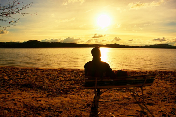Zmęczony młody człowiek siedzieć na starej drewnianej ławeczce nad morzem. Archiwalne zdjęcie stonowanych - Zdjęcie, obraz