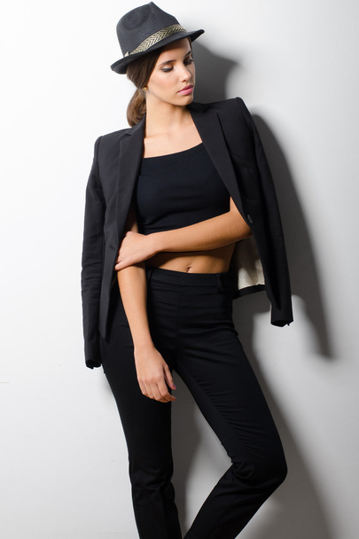 Beautiful fashionable girl in black clothes leaning on white wall - Foto, imagen