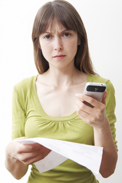 Young Woman With Mobile Phone And Bill Looking Worried - Foto, immagini