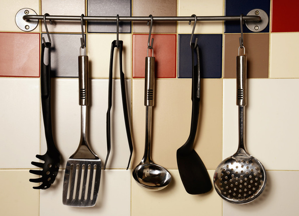 Küchenutensilien hängen an einer Wand aus farbigen Fliesen - Foto, Bild