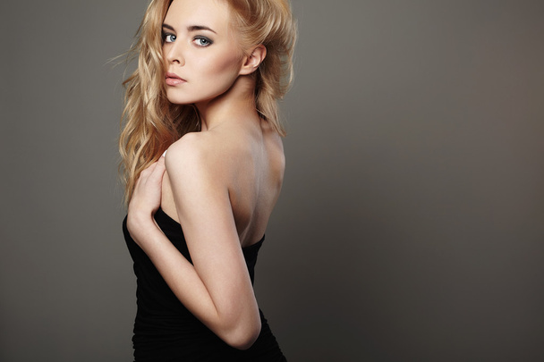 beautiful young woman with blond hair. Girl in black dress on grey background - Photo, Image