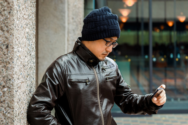 Азиат в коричневой куртке проверяет сообщение со своего смартфона
 - Фото, изображение