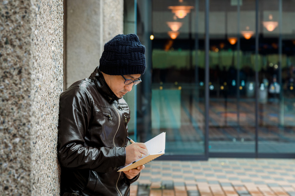 Een Aziatische Man in een bruine jas met een klein notitieboekje  - Foto, afbeelding