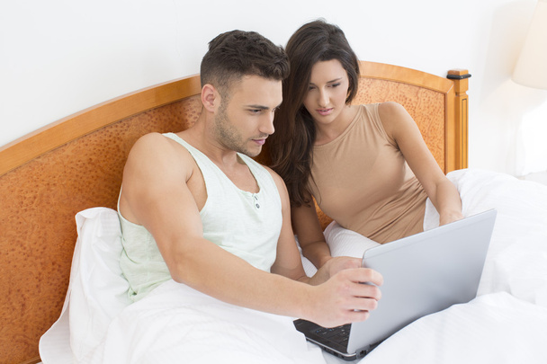 Couple in bed looking at laptop together - 写真・画像