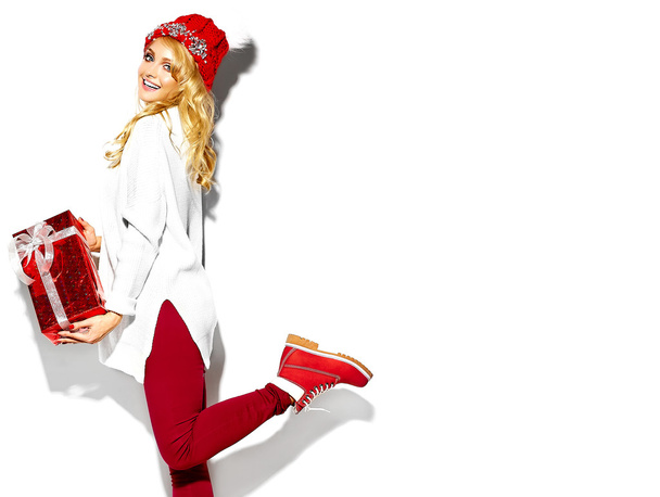 portrait of beautiful happy sweet smiling blonde woman girl holding in her hands big Christmas gift box in casual red hipster winter clothes, in white warm sweater standing on one leg - Zdjęcie, obraz
