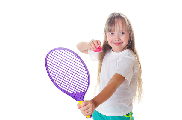 Tyttö pitää kädessään tennismailaa pallolla ja hymyilee.
 - Valokuva, kuva