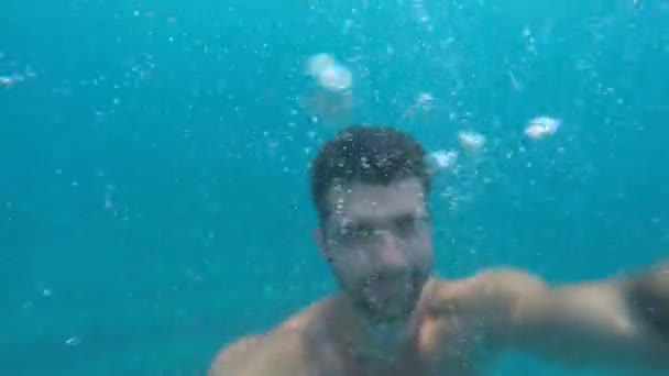 水中の男性。一方、ダイビングとスイミング、彼の敬礼、笑顔し、波します。カメラは、手でその自画像です。. - 映像、動画