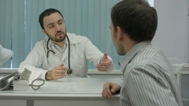 Мужской бородатый врач в клинике измеряет пульс клиента-мужчины
. - Кадры, видео