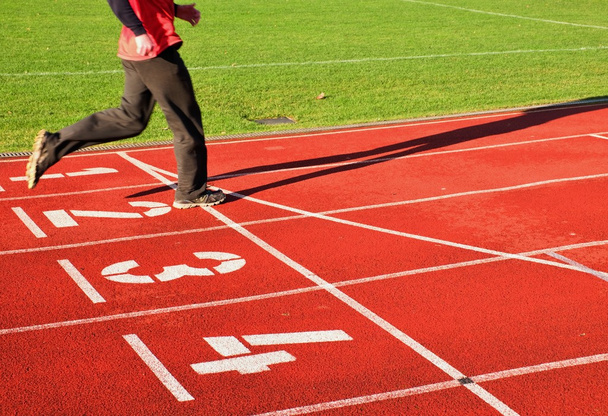 Piros futó versenypálya, a stadion, a két futó lábak melegítőben nadrág  - Fotó, kép