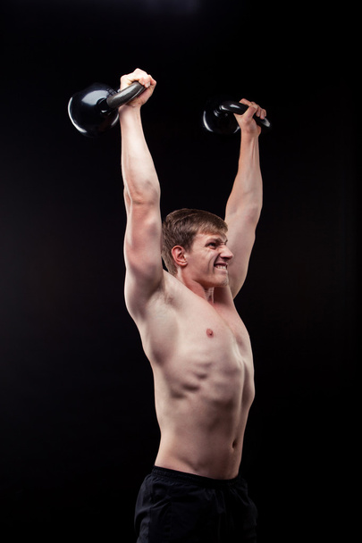 Handsome muscular guy with kettlebells isolated on black background - Foto, Imagem