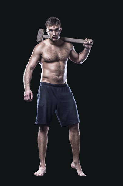 Sportsman with a sledgehammer next to tire isolated on black - Photo, image