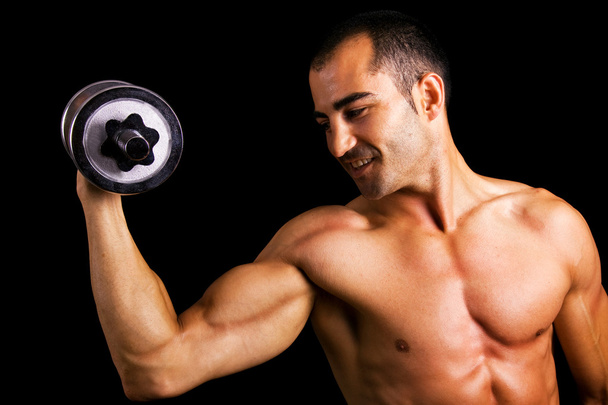 Young muscular man lifting dumbbells against black background - Foto, afbeelding