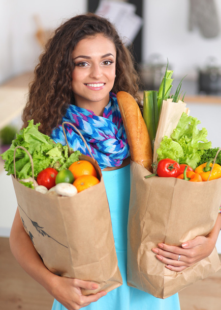 Sebzeli alışveriş poşeti taşıyan genç bir kadın mutfakta duruyor.. - Fotoğraf, Görsel